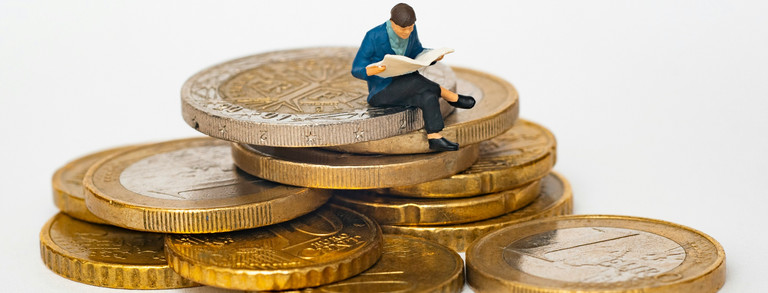 Miniature figurine of a seated person reading the newspaper placed on a stack of euro coins